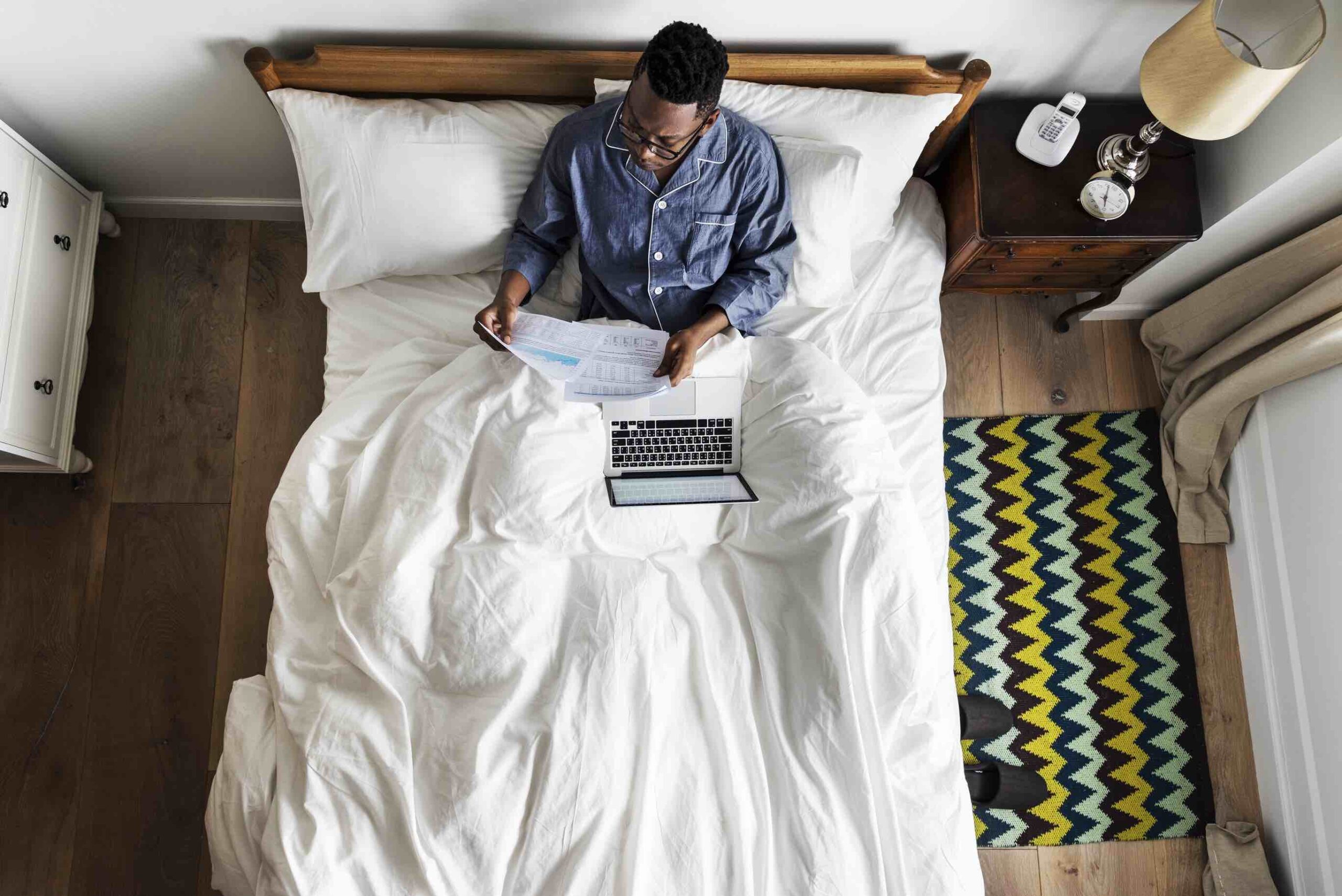 Um homem numa cama a trabalhar no seu computador portátil.