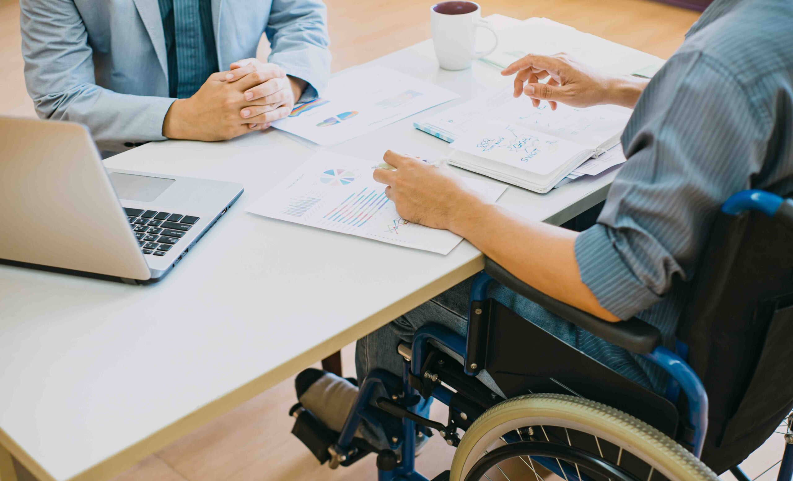 Two people — one sitting in a wheelchair — are looking over some papers.