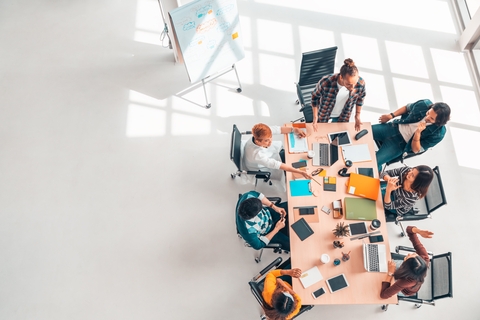 Coworkers around a table with notebooks, paper, and a devices.