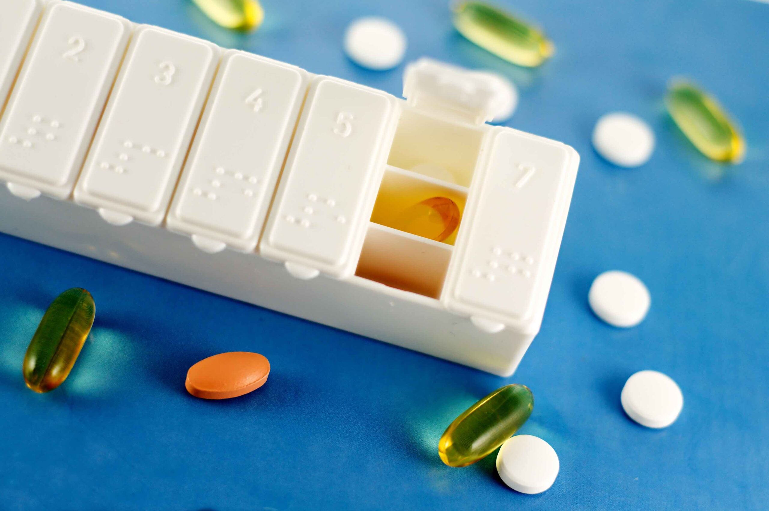 A pill organizer with pills strewn around it.