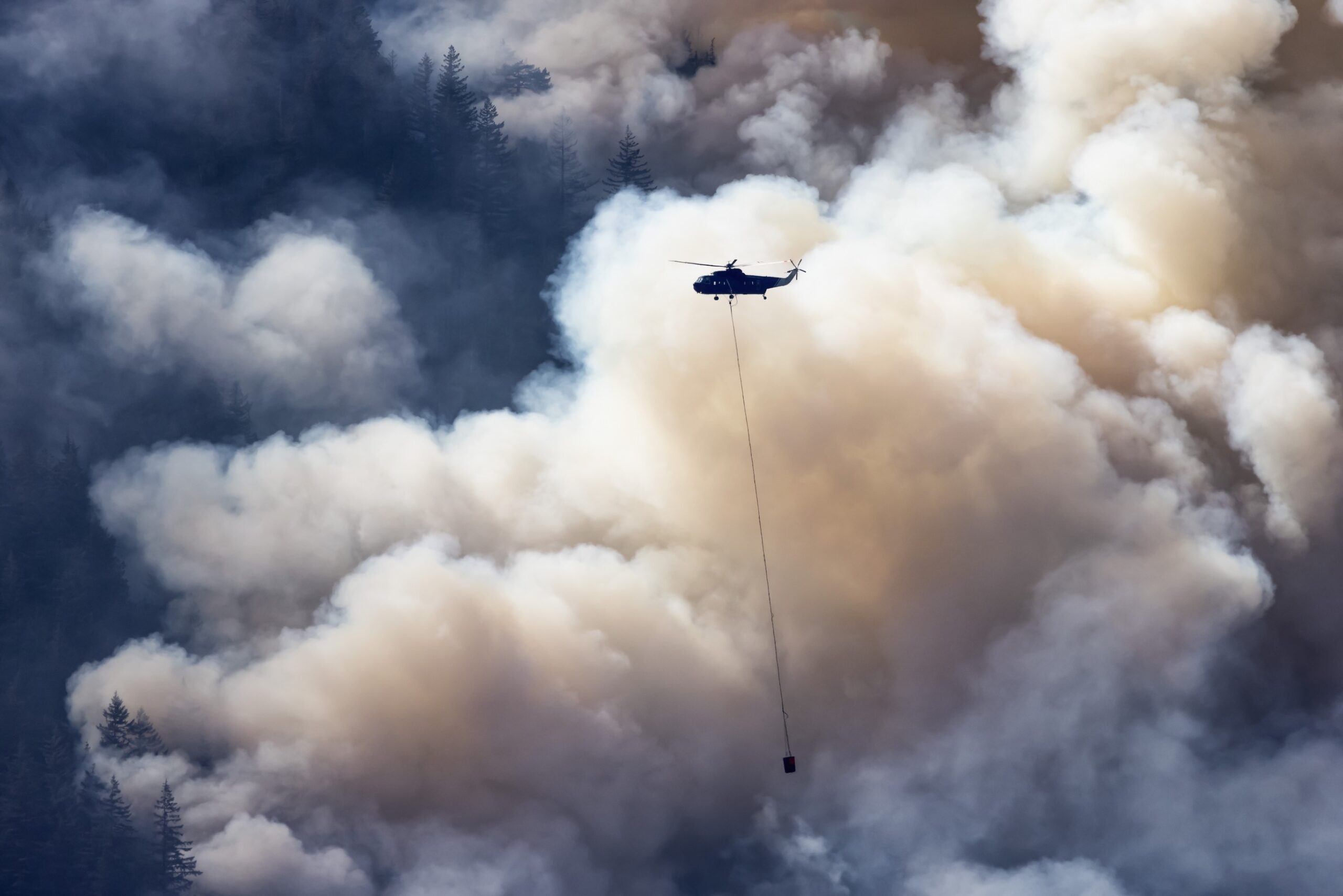 Ein Hubschrauber fliegt über dem Rauch eines Waldbrandes.