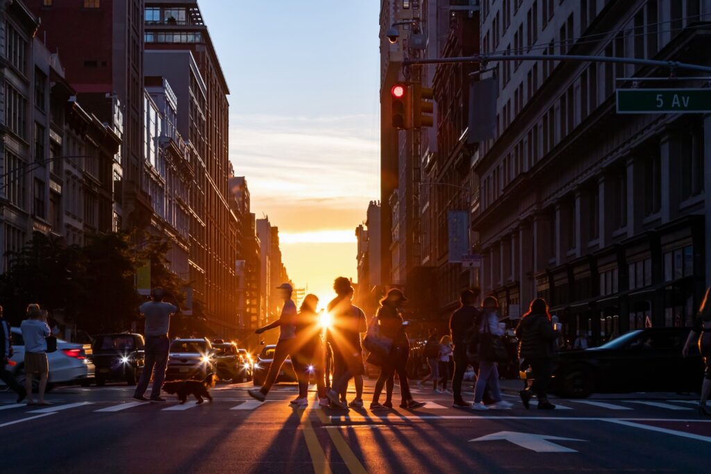 Siluet pria dan wanita yang sedang menyeberangi jalan ramai di Midtown Manhattan, Kota New York, dengan latar belakang sinar matahari